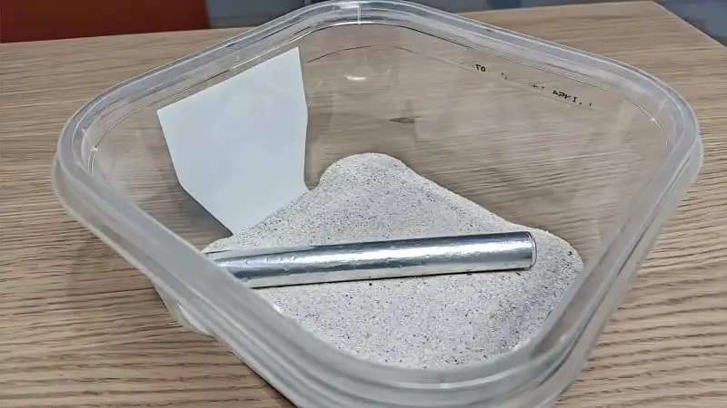 Finished tubs and tubes setup with a foil-wrapped test tube on white sand inside an oiled plastic tub