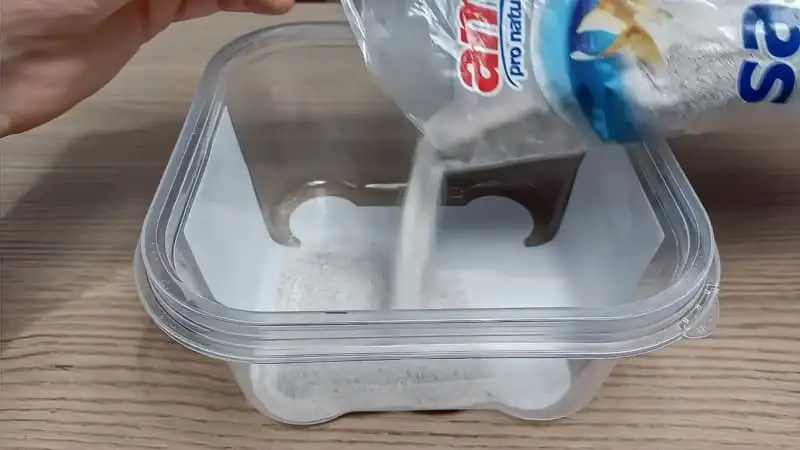 Pouring sterilized white aquarium sand into a plastic tub to create the substrate of an outworld